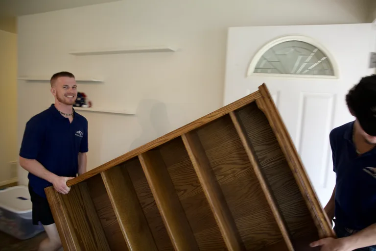 Two RiverHills movers carrying a large wooden bookshelf through a home